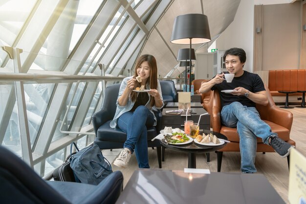 Seduta asiatica delle coppie e salotto dell&#39;aeroporto della locanda di eatting quando aspettano il volo