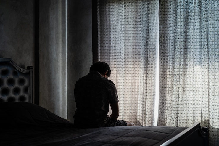 Seduta depressa e sollecitata del giovane solo nella camera da letto scura, concetto negativo di emozione