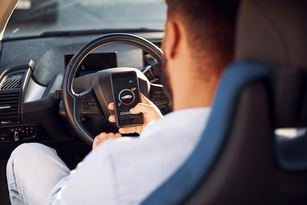 Seduto all'interno del processo di ricarica del monitoraggio del veicolo Giovane uomo elegante è con auto elettrica