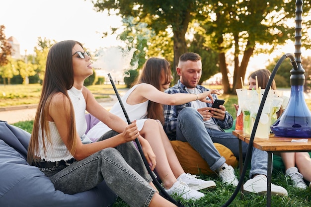 Seduto in poltrona borse e fumare narghilè Un gruppo di giovani organizza una festa nel parco durante il giorno d'estate