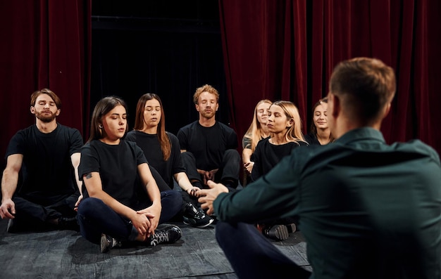 Seduto per terra Gruppo di attori in abiti scuri durante le prove a teatro