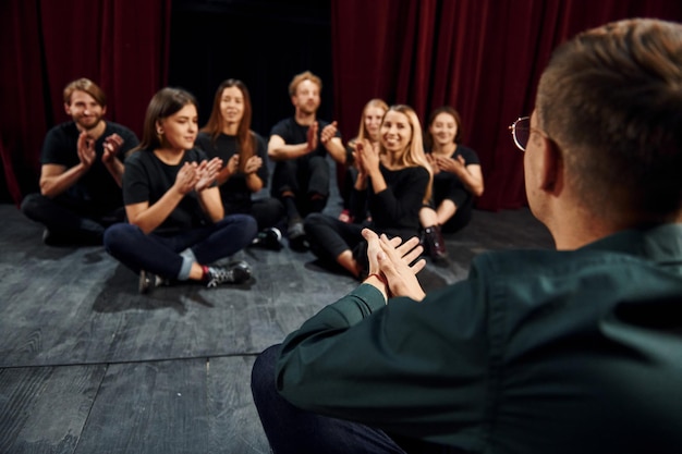 Seduto per terra Gruppo di attori in abiti scuri durante le prove a teatro