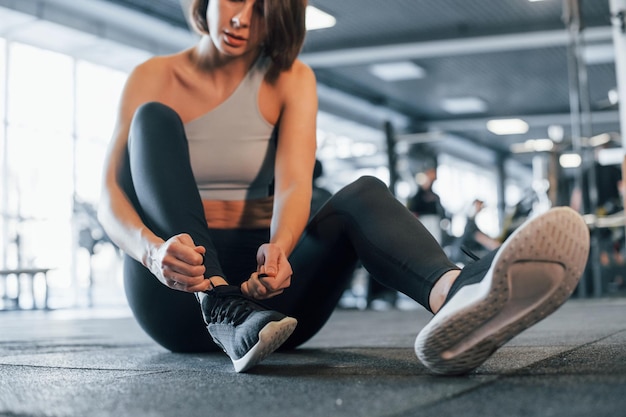 Seduto per terra Una donna in abiti sportivi con un fisico snello è in palestra