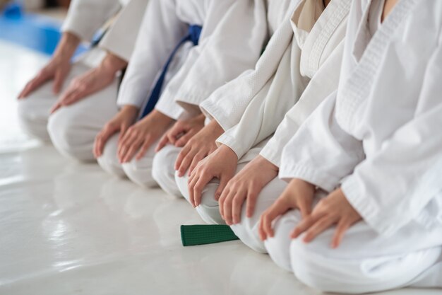 Seduto sul pavimento. Bambini che indossano un kimono bianco seduti sul pavimento e ascoltano l'allenatore