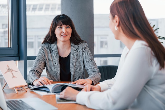 Seduto vicino al tavolo Due donne in abiti formali sono al chiuso nell'ufficio moderno lavora insieme