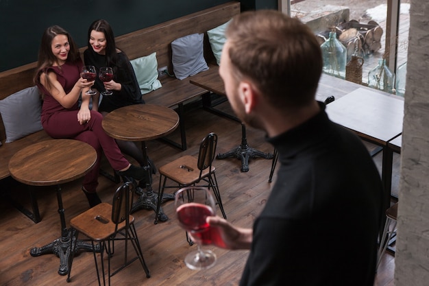 Seduzione femminile. Pettegolezzi sul maschio. Donne civettuole nel bar a fuoco sullo sfondo, uomo irriconoscibile con vino, concetto di flirt