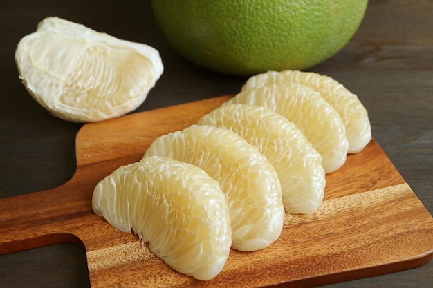 Segmenti di frutta fresca sbucciata del pomelo allineati sul tagliere di legno