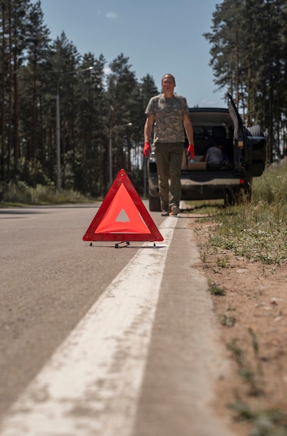 Segnale di attenzione triangolare sulla strada vicino all'auto rotta con l'autista che si dirige verso di essa