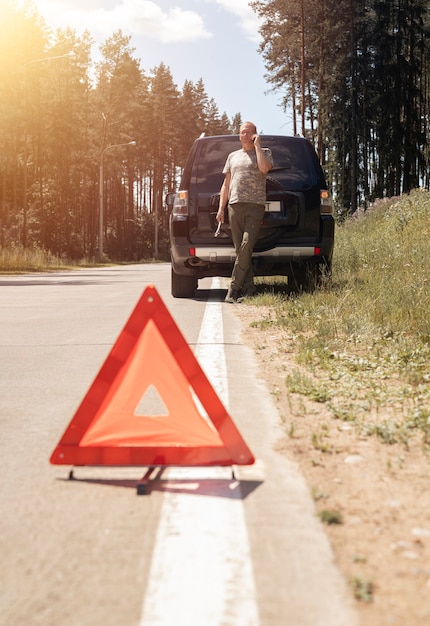 Segnale di attenzione triangolo rosso sulla strada dopo la rottura dell'auto in viaggio e autista che parla su una chiamata al cellulare...