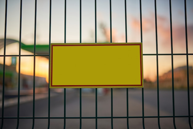 Segnale di pericolo giallo vuoto al recinto, città blured al tramonto