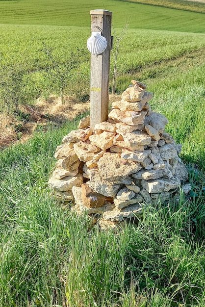 Segno del Camino de Santiago con conchiglia appesa al palo su un mucchio di pietre