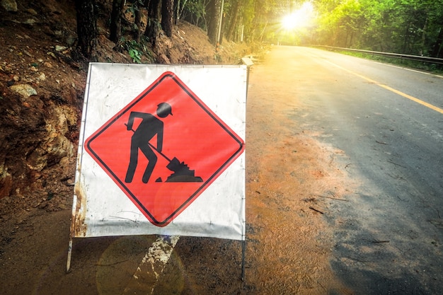 Segno della costruzione rossa sulla strada campestre con gli alberi sul fondo del bordo della strada