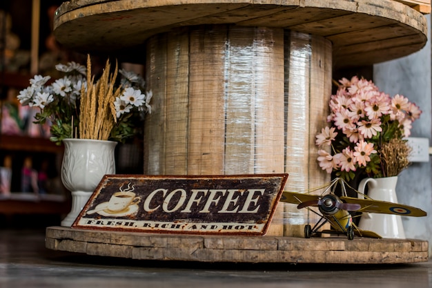 Segno di caffè, elicottero giocattolo e fiori finti in un vaso che viene visualizzato su un tavolo di legno.