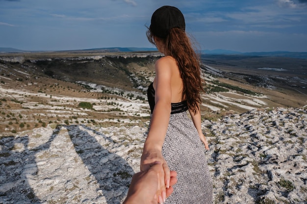 Seguimi con una giovane donna che guida per mano un viaggiatore in una zona montuosa Paesaggio montano sotto il cielo