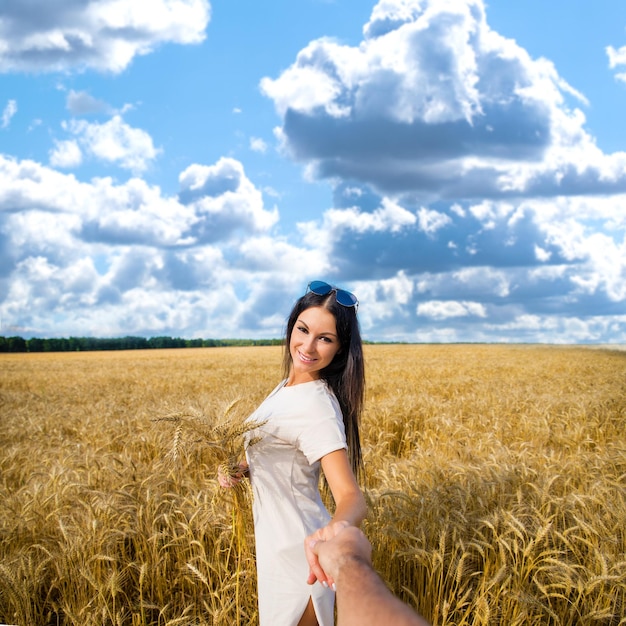 Seguitemi Una bella giovane donna sexy tiene la mano di un uomo in un campo di grano