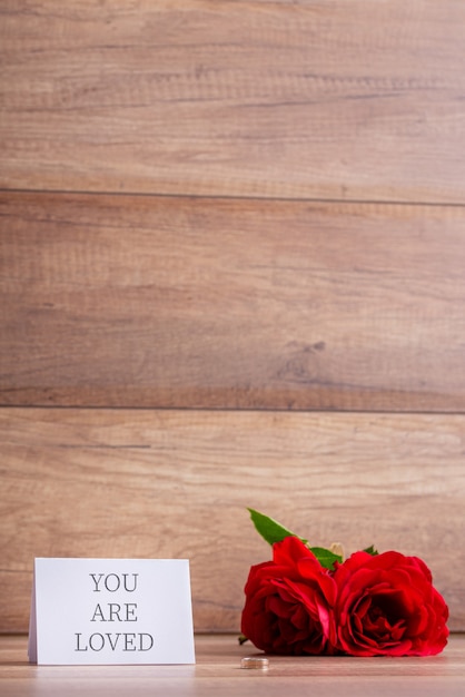 Sei amato biglietto di auguri accanto a due rose rosse e anello di fidanzamento