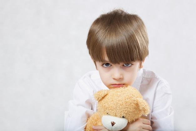 Sei anni ragazzo seduto sulla sedia con peluche orsacchiotto. Avvicinamento