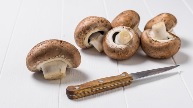 Sei grandi funghi e un coltello su un tavolo di legno bianco. Cibo vegetariano. Funghi coltivati artificialmente.