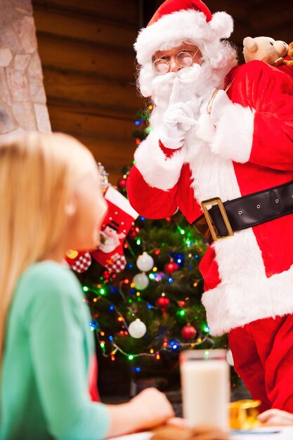 Sei tu Babbo Natale? Bambina sorpresa che guarda il vero Babbo Natale che tiene in mano un sacco con dei regali