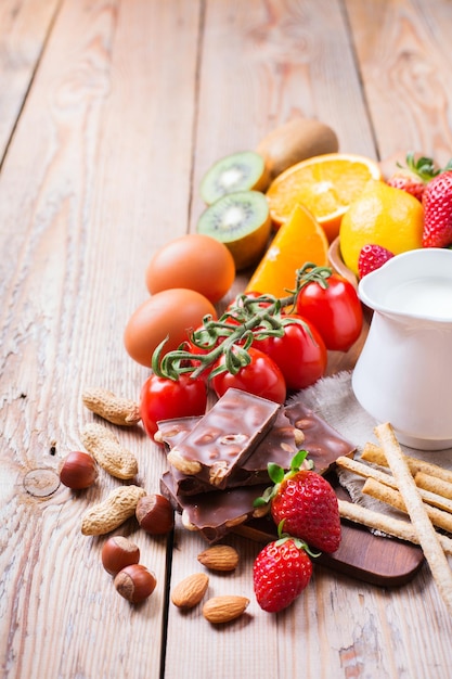 Selezione di alimenti per allergie arancia succo di agrumi latte pomodoro rosso fragola kiwi uova cioccolato noci pane glutine prodotti lattiero-caseari su un rustico tavolo in legno copia spazio sfondo