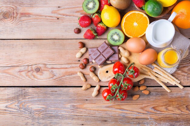 Selezione di alimenti per allergie arancia succo di agrumi latte pomodoro rosso fragola kiwi uova cioccolato noci pane glutine prodotti lattiero-caseari su un tavolo di legno rustico copia spazio sfondo vista dall'alto piatto lay