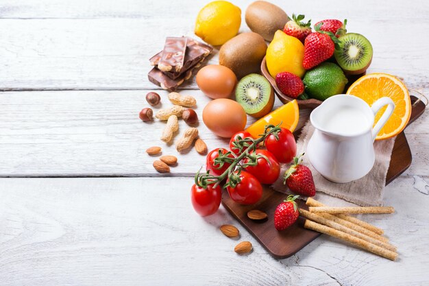 Selezione di alimenti per allergie arancia succo di agrumi latte pomodoro rosso fragola kiwi uova cioccolato noci pane glutine su un tavolo di legno rustico Copia spazio sullo sfondo