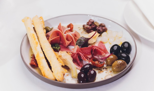 Selezione di antipasti a base di carne Salami prosciutto bastoncini di pane baguette olive e pomodori secchi selettivi