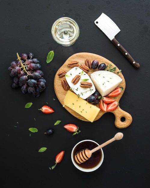 Selezione di antipasti di formaggio o set di snack a base di vino Varietà di uva da formaggio noci pecan fragola e miele su tavola rotonda di legno su sfondo nero