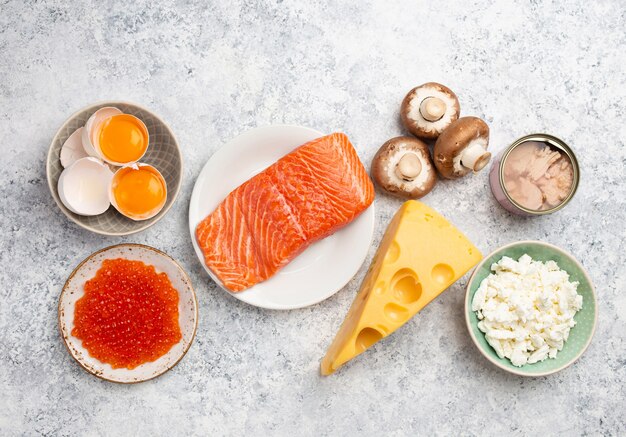 Selezione di fonti naturali di vitamina D: salmone fresco, caviale, formaggio, funghi, tonno, uova su sfondo di pietra bianca vista dall'alto. Cibi e prodotti assortiti ricchi di vitamina D, dall'alto