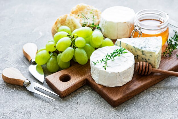 Selezione di formaggi, miele e uva su sfondo grigio cemento