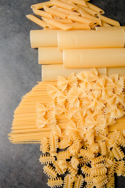 Selezione di pasta secca mista su sfondo nero. Varietà di tipi e formati di pasta italiana. Sfondo di pasta cruda.
