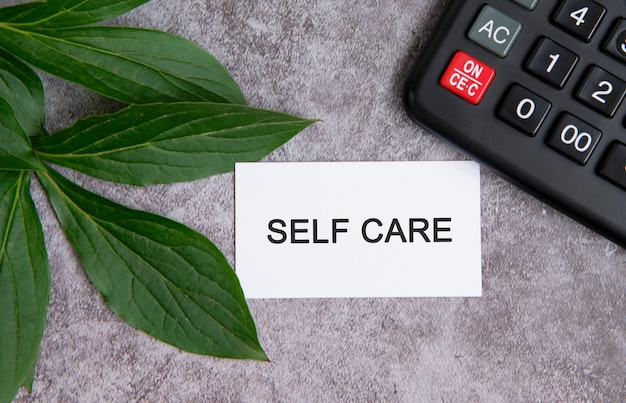 SELF CARE - testo su un tavolo di cemento grigio con una calcolatrice e foglie verdi