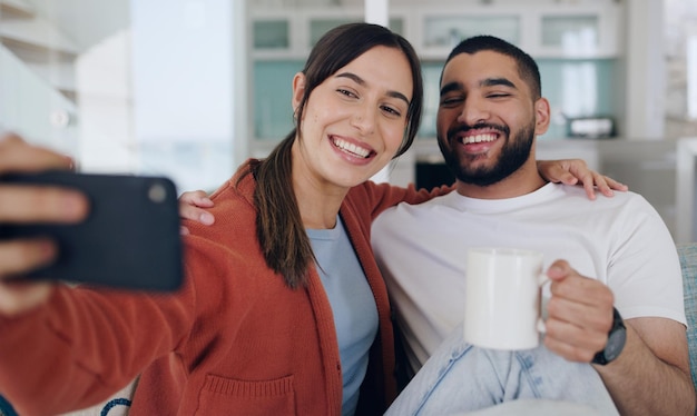 Selfie a casa e sorriso di coppia sul divano per post sui social media vlog online e internet con caffè Incontri mattina e uomo e donna felici scattano una foto per aggiornare il legame e rilassarsi in soggiorno