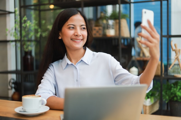 Selfie asiatico della donna con il telefono cellulare nel sorriso del caffè della caffetteria e nel fronte felice