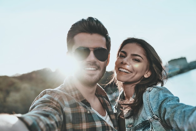 Selfie con l'innamorato. Autoritratto di bella giovane coppia che abbraccia e che guarda l'obbiettivo