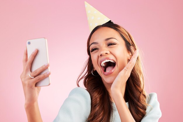 Selfie di compleanno ed eccitato con una donna in studio su sfondo rosa per la celebrazione di un evento Telefono social media e festa con una giovane donna attraente che celebra un'occasione speciale