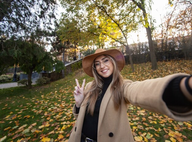 Selfie ritratto di una giovane donna divertente sullo sfondo di foglie cadute nel parco. Tempo d'autunno