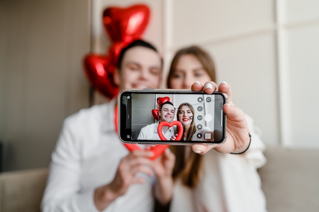 Selfie sullo schermo del telefono delle belle coppie a casa sul divano con il cuore