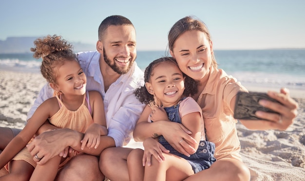 Selfie telefono e famiglia sorriso in spiaggia divertendosi ridere e divertirsi sulla sabbia in estate Genitori e figli felici che si uniscono in vacanza al mare e fine settimana allegri con il cellulare