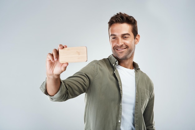 Selfie time Foto in studio di un giovane allegro che fa un autoritratto con il suo cellulare mentre si trova su uno sfondo grigio
