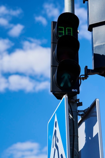 Semaforo verde della strada per i pedoni contro i segnali stradali dell'automobile del cielo blu