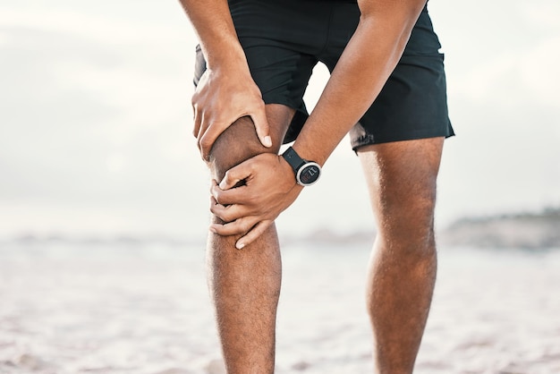 Sembra non più correre Ripresa ritagliata di un atleta maschio irriconoscibile che si tiene il ginocchio dolorante mentre si allena sulla spiaggia