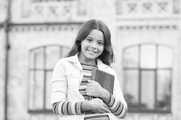 Sembra sapere tutto Ragazza intelligente tenere il libro all'aperto Ragazza felice torna a scuola Ragazza della scuola elementare Bambina con i capelli lunghi in stile casual Giornata della conoscenza Scuola e istruzione