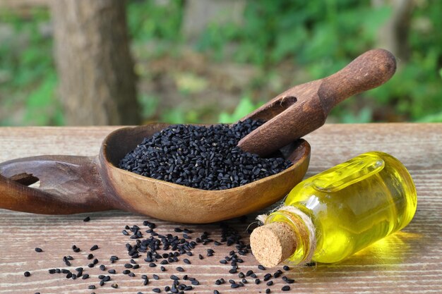 Semi di cumino nero e olio essenziale con ciotola e pala o cucchiaio di legno Nigella Sativa