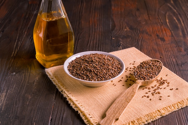 Semi di lino e olio marroni di lino su fondo di legno, vista superiore.