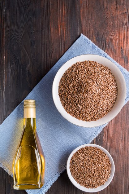 Semi di lino marroni e olio di lino su superficie di legno, superficie piana.