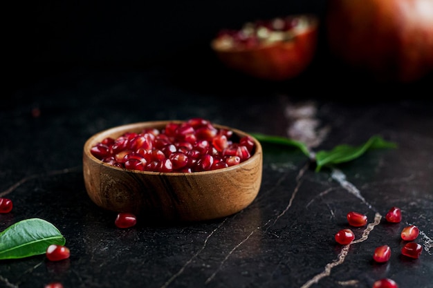 Semi di melograno in ciotola di legno con semi su tavola nera con frutti di melograno sullo sfondo