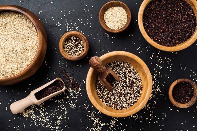 Semi di quinoa bianchi, neri e misti in una ciotola di bambù su un tavolo di pietra nera. Lay piatto con copia spazio.