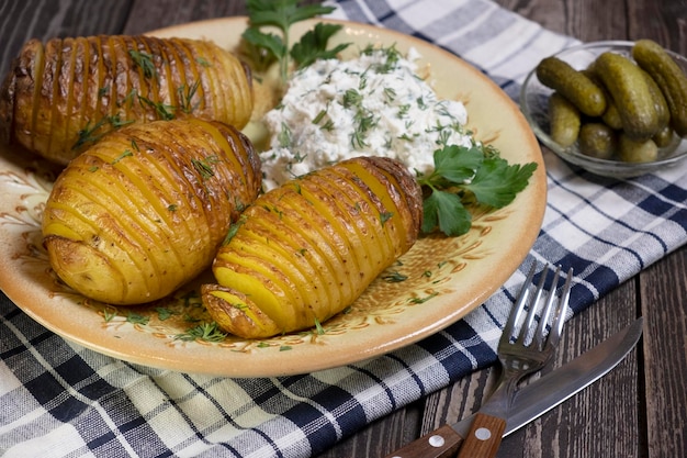 Semplice cibo rustico patate al forno con ricotta ed erbe aromatiche cetrioli sottaceto e un tovagliolo su uno sfondo di legno scuro