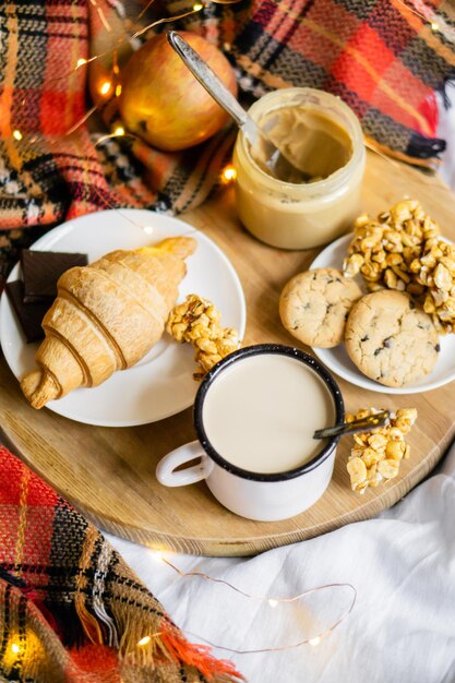 Semplice colazione casalinga di campagna a letto caffè con latte e pasticceria fatta in casa su coperta a quadri